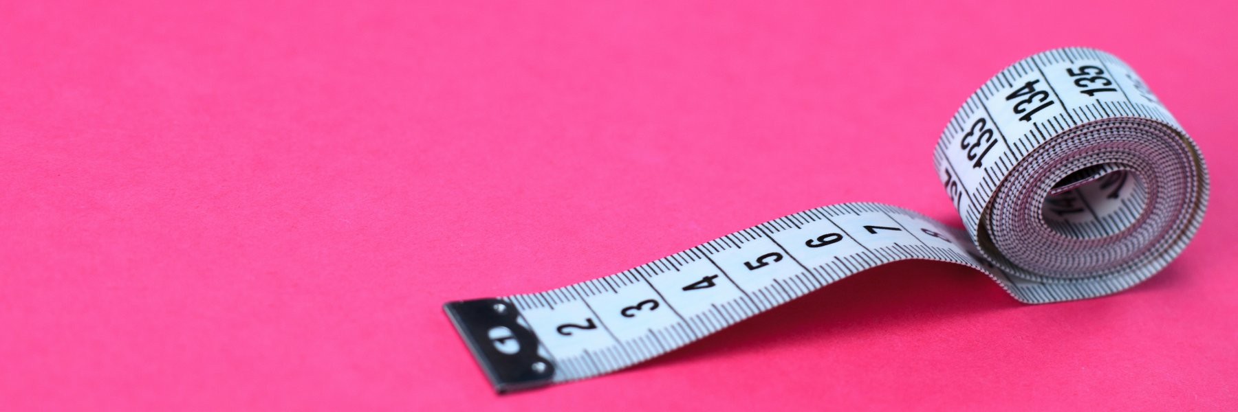 Rolled up white tape measure with pink background.