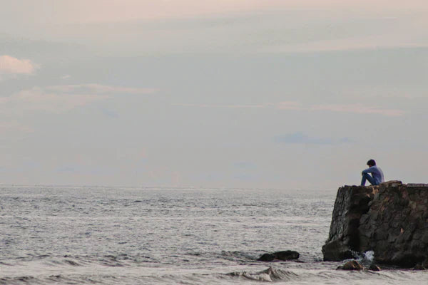 A stressed bloke sitting on a rock by the sea. His sex drive is low due to the stress.